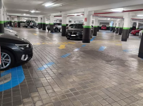 Wide view of the interior of Parking Garaje Ronda de Atocha: the columns colored black, green, and white, while the arrows on the floor are yellow and indicate the direction of travel. 